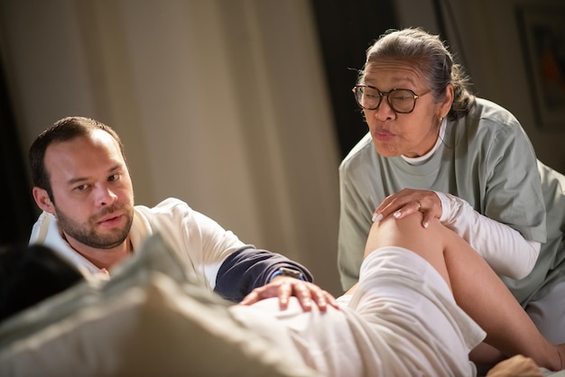 Foto gratuita mujer dando a luz en casa con esposo y partera. hombre barbudo y mujer asiática ayudando, tranquilizando a la futura madre. embarazo, concepto de parto en casa