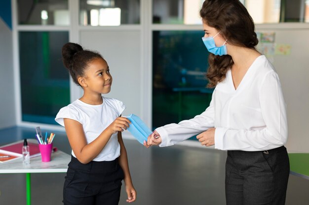 Mujer dando una mascarilla médica a un estudiante