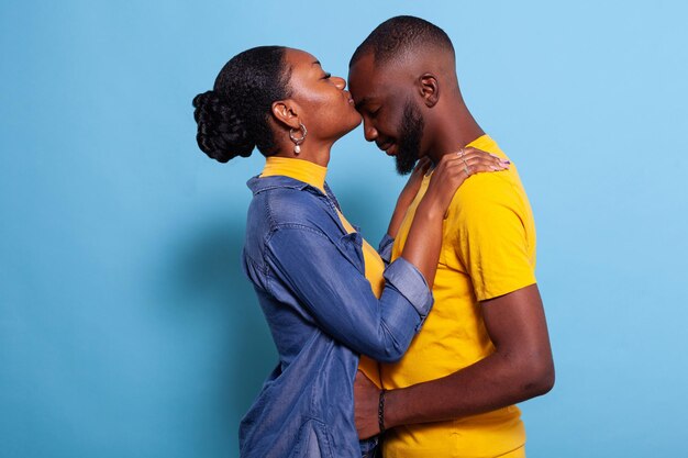 Mujer dando novio un beso en la frente para expresar amor frente a la cámara. Personas en relación que muestran afecto y pasión con abrazos y besos. Pareja romántica con emociones felices.