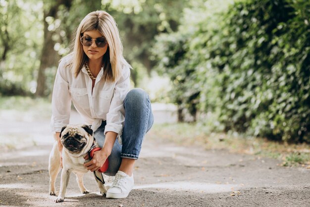 Mujer dando un paseo en el parque con su mascota perro pug