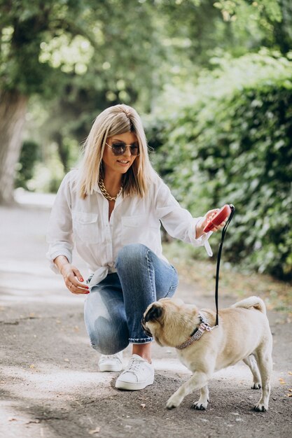 Mujer dando un paseo en el parque con su mascota perro pug