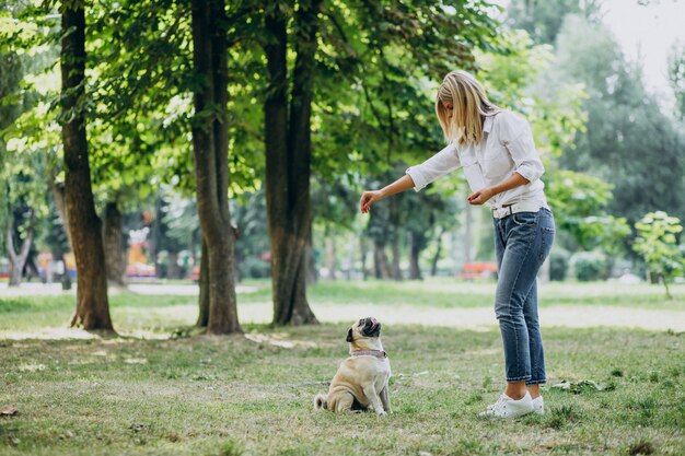 Mujer dando un paseo en el parque con su mascota perro pug