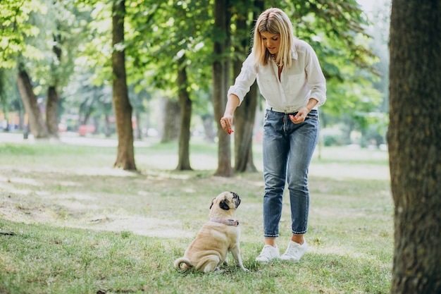 Mujer dando un paseo en el parque con su mascota perro pug