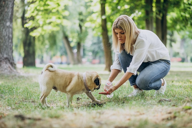 Mujer dando un paseo en el parque con su mascota perro pug