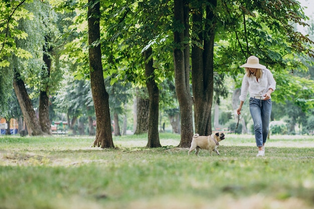 Mujer dando un paseo en el parque con su mascota perro pug