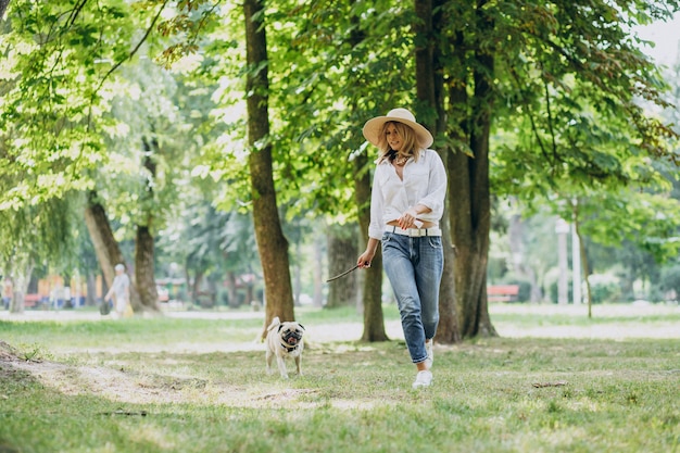 Mujer dando un paseo en el parque con su mascota perro pug