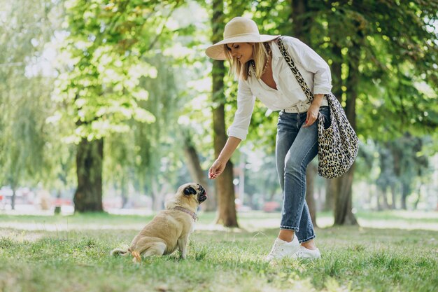 Mujer dando un paseo en el parque con su mascota perro pug