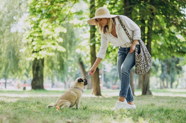 Mujer dando un paseo en el parque con su mascota perro pug