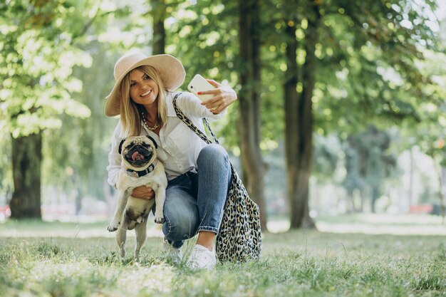 Mujer dando un paseo en el parque con su mascota perro pug