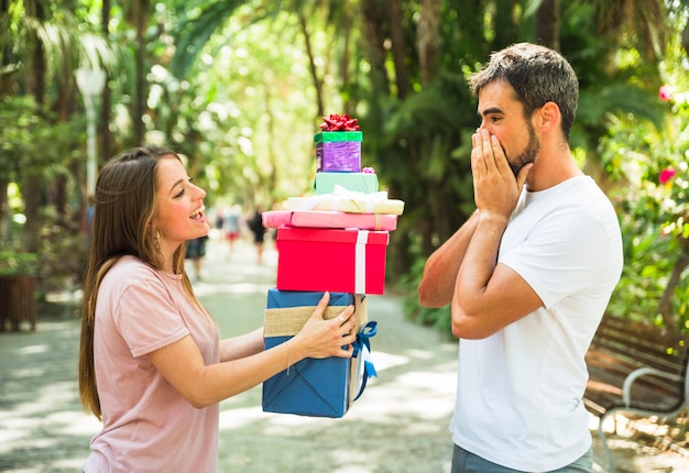 Mujer dando pila de regalos a su novio sorprendido