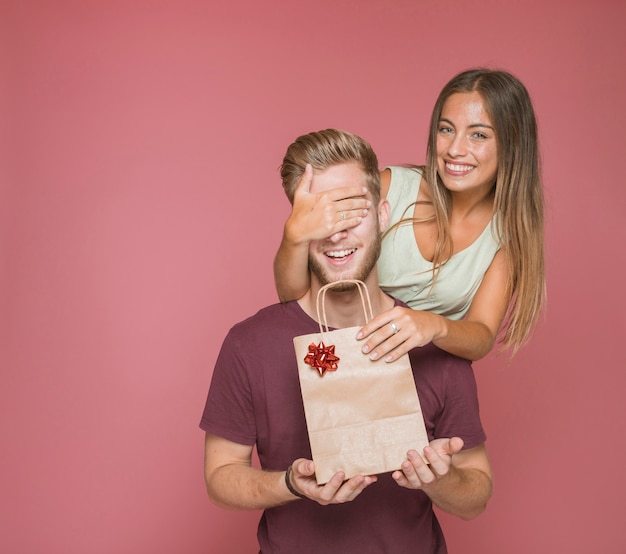 Mujer dando un regalo de bolsa de compras a su novio cubriendo sus ojos