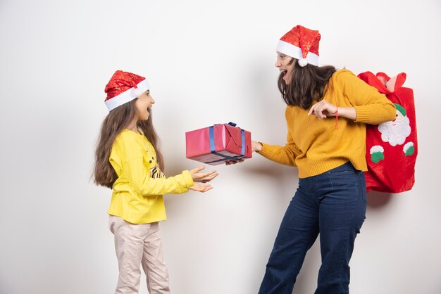 Mujer dando un regalo a la niña con sombrero rojo de Santa Claus.