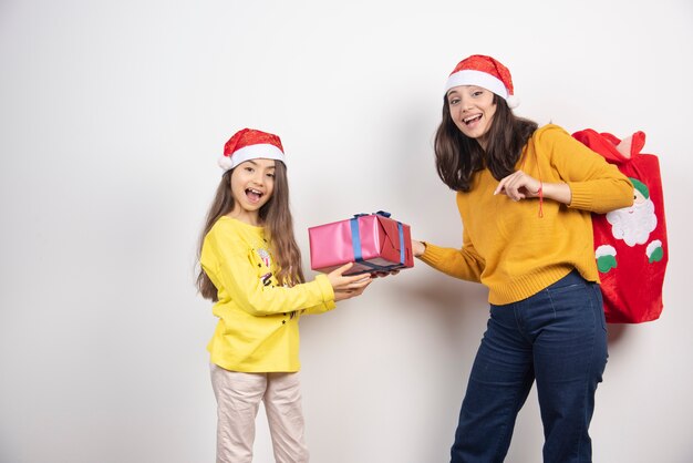 Mujer dando un regalo a la niña con sombrero rojo de Santa Claus.