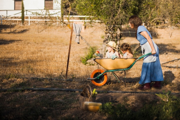 Foto gratuita mujer dando a sus hijos paseo en carretilla