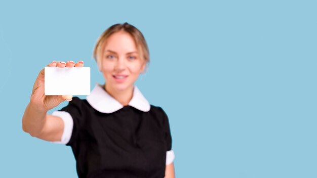 Mujer Defocused que muestra la tarjeta de visita blanca en blanco delante del fondo azul
