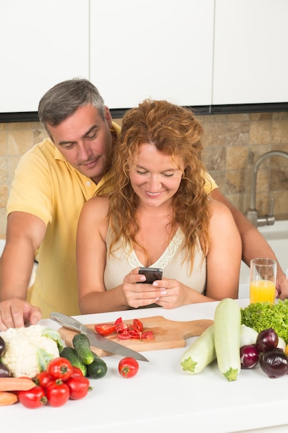 La mujer dejó de cocinar para leer el mensaje en su teléfono móvil. El hombre está detrás de ella mirando el teléfono.