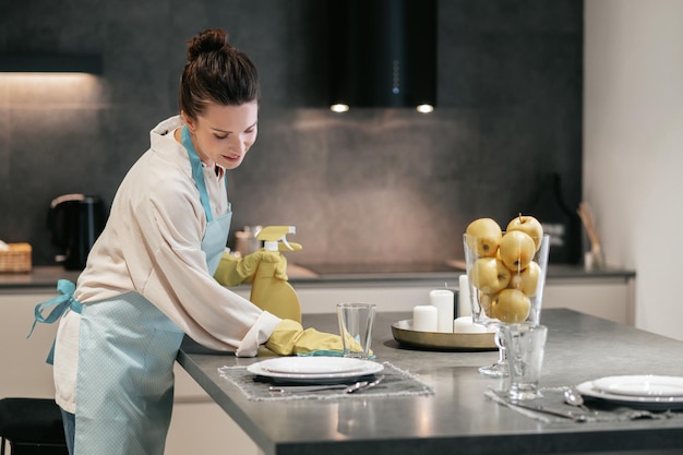 Una mujer con delantal limpiando la mesa en la cocina.