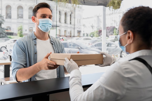 Mujer con delantal ofreciendo comida para llevar empaquetada al cliente masculino