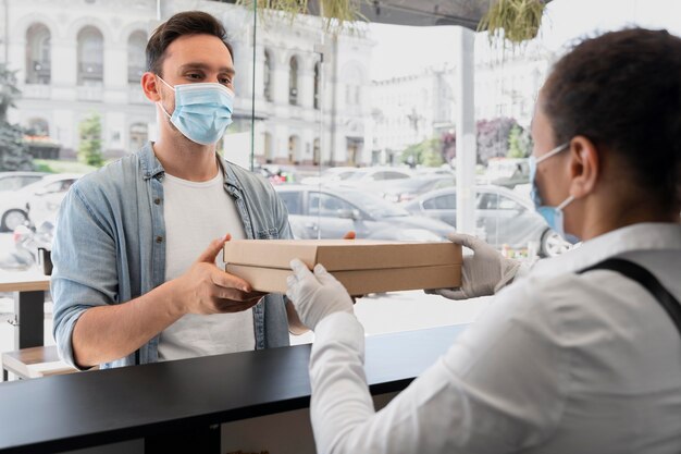 Mujer con delantal ofreciendo comida para llevar empaquetada al cliente masculino