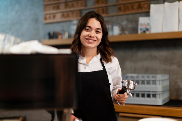 Mujer con delantal posando con componente de máquina de café