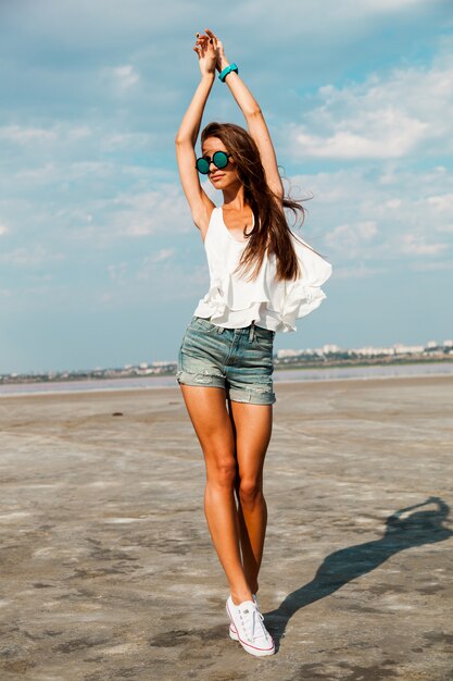 Mujer delgada en camiseta blanca posando cerca de la playa.