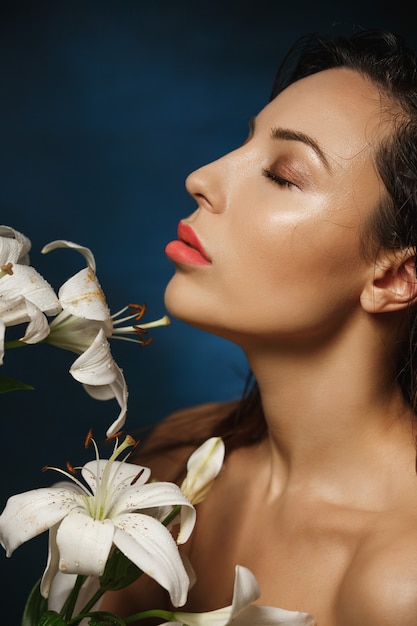 Foto gratuita mujer delgada desnuda posando con los ojos cerrados, sosteniendo flores de lirio.