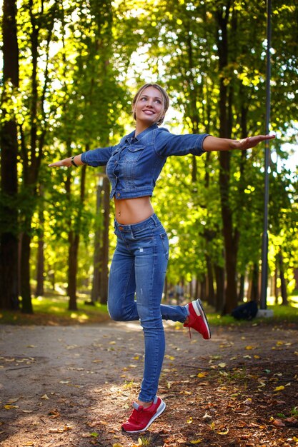 Mujer delgada feliz con ropa de mezclilla posando en un parque natural verde.