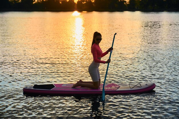 Mujer delgada flotando en el tablero de sup durante la puesta de sol