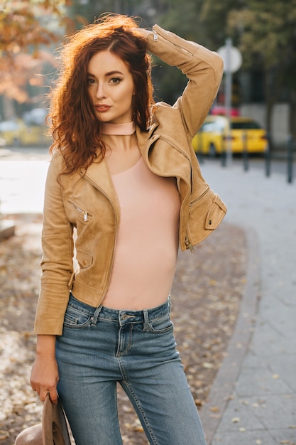 Mujer delgada de jengibre juega con su cabello mientras posa en día de otoño