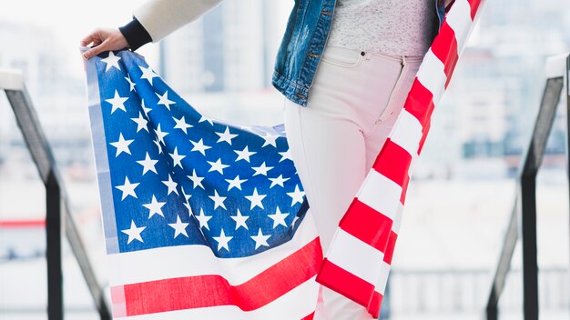 Mujer delgada que sostiene la bandera estadounidense detrás de las piernas