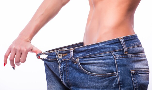 Mujer delgada tirando de jeans de gran tamaño. Concepto de pérdida de peso. Aislado en la pared blanca