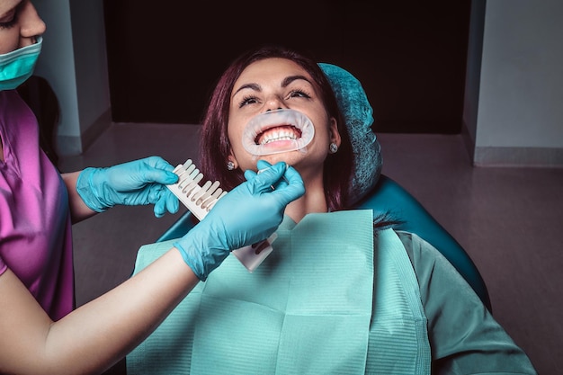 Foto gratuita una mujer dentista comprueba el nivel de blanqueamiento dental con el color de un dentista en el consultorio del dentista.