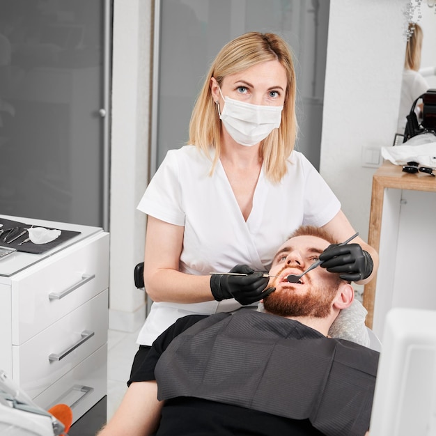 Mujer dentista examinando los dientes del hombre en el consultorio dental