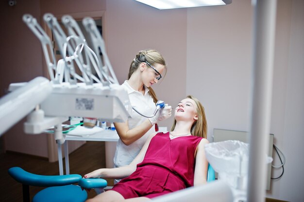 Mujer dentista con gafas especiales tratando los dientes de su paciente con instrumentos dentales