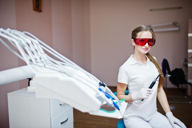 Mujer dentista con gafas rojas especiales tratando los dientes de su paciente con instrumentos dentales