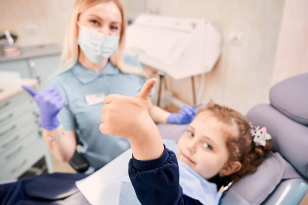 Mujer dentista y linda niña dando pulgares arriba