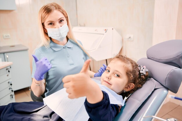 Mujer dentista y linda niña dando pulgares arriba