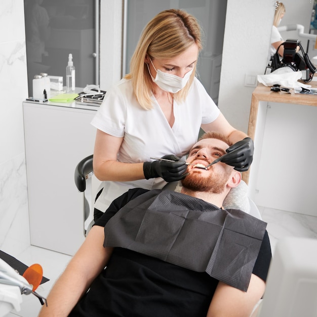 Foto gratuita mujer dentista en el trabajo durante el chequeo de los dientes del hombre en el consultorio del dentista