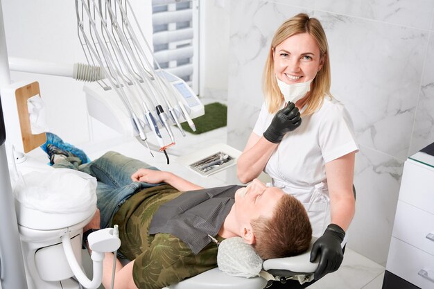 Mujer dentista en el trabajo con el paciente examinando sus dientes con herramientas dentales