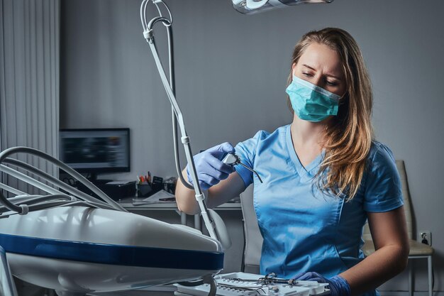 Mujer dentista con uniforme y máscara sentada en una silla en su lugar de trabajo en una clínica dental.