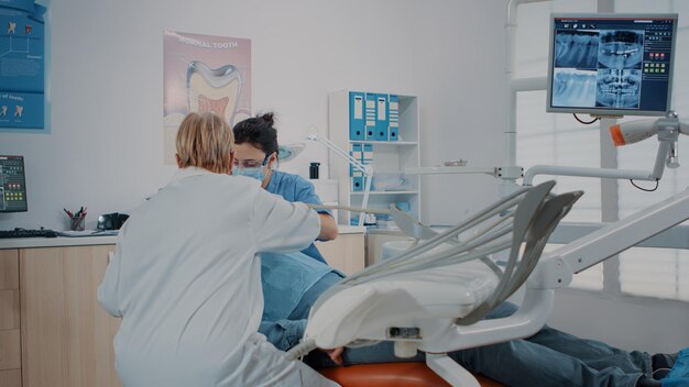 Mujer dentista usando un instrumento para hacer un procedimiento de perforación, tratando a un paciente con dolor de muelas. Estomatólogo que examina la dentadura postiza con herramientas dentales para la inspección del cuidado bucal. inspección de odontología