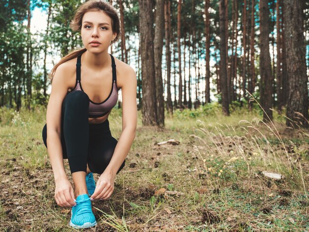 Mujer deportiva atar cordones de los zapatos en los zapatos para correr antes de la práctica en el bosque