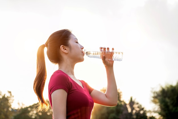 Mujer deportiva bebiendo agua en la luz del sol.