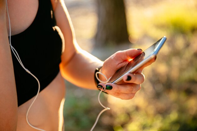 mujer deportiva en camiseta negra con un teléfono móvil mientras escucha música