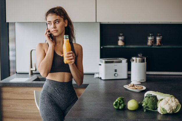 Mujer deportiva en la cocina mediante teléfono móvil