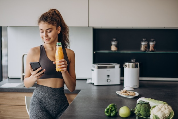 Mujer deportiva en la cocina mediante teléfono móvil