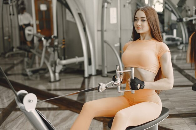 Mujer deportiva entrenando su espalda con máquina de pesas. Vistiendo traje naranja.