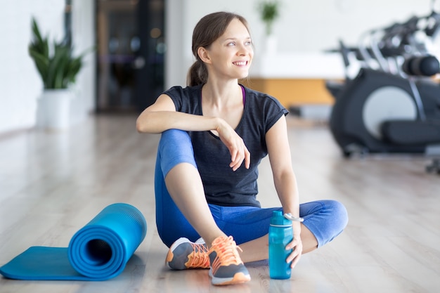 Mujer deportiva feliz en el suelo con la estera y el agua