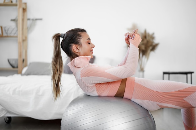 Mujer deportiva haciendo ejercicios de abdominales en pelota de fitness en casa