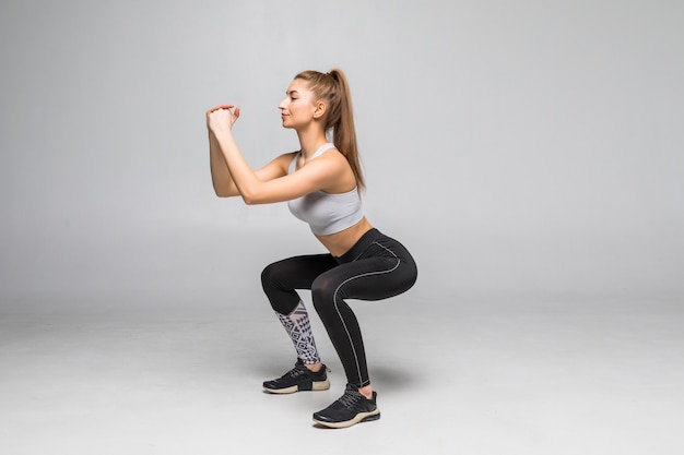 Mujer deportiva haciendo sentadillas. Mujer fitness muscular en ropa deportiva militar aislada en la pared blanca. Concepto de fitness y estilo de vida saludable